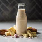 Glass bottle filled with homemade peppermint white chocolate mocha syrup made with real white chocolate, sitting on a white countertop with a herringbone backsplash.